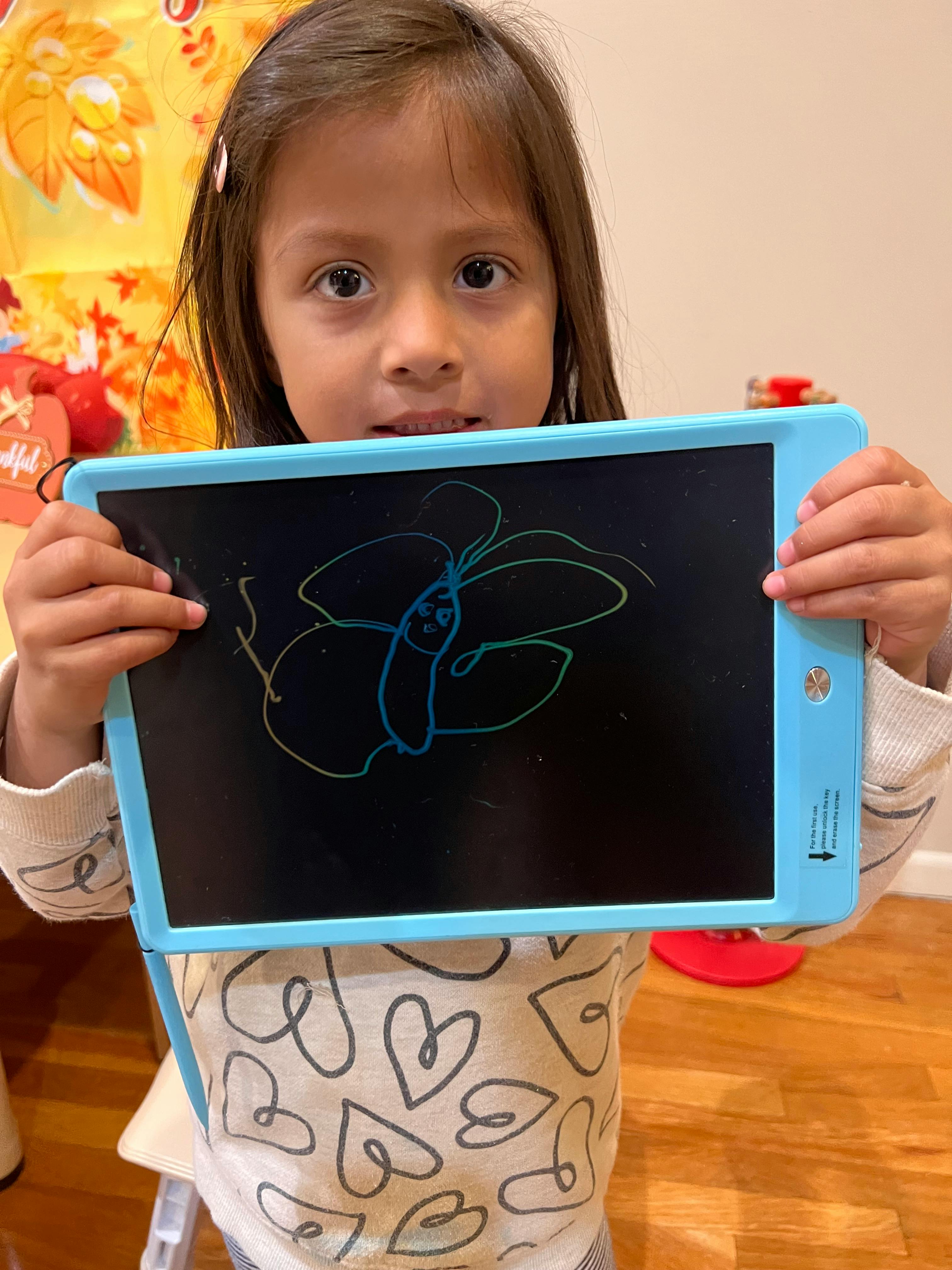 Child holding up a blue drawing tablet with a flower drawing