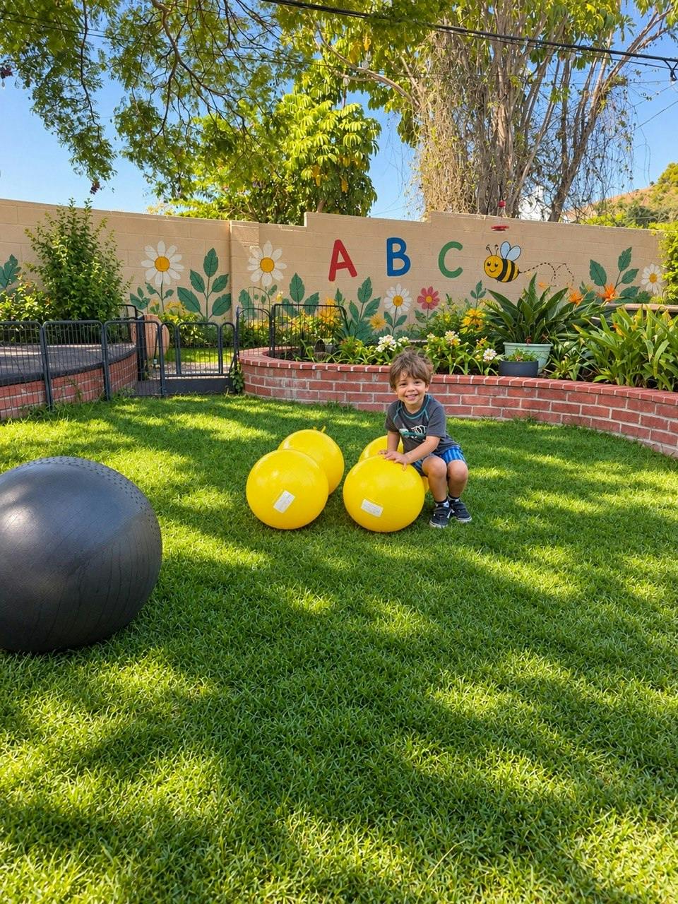 Child sitting on yellow balls in a backyard with an ABC mural on the wall
