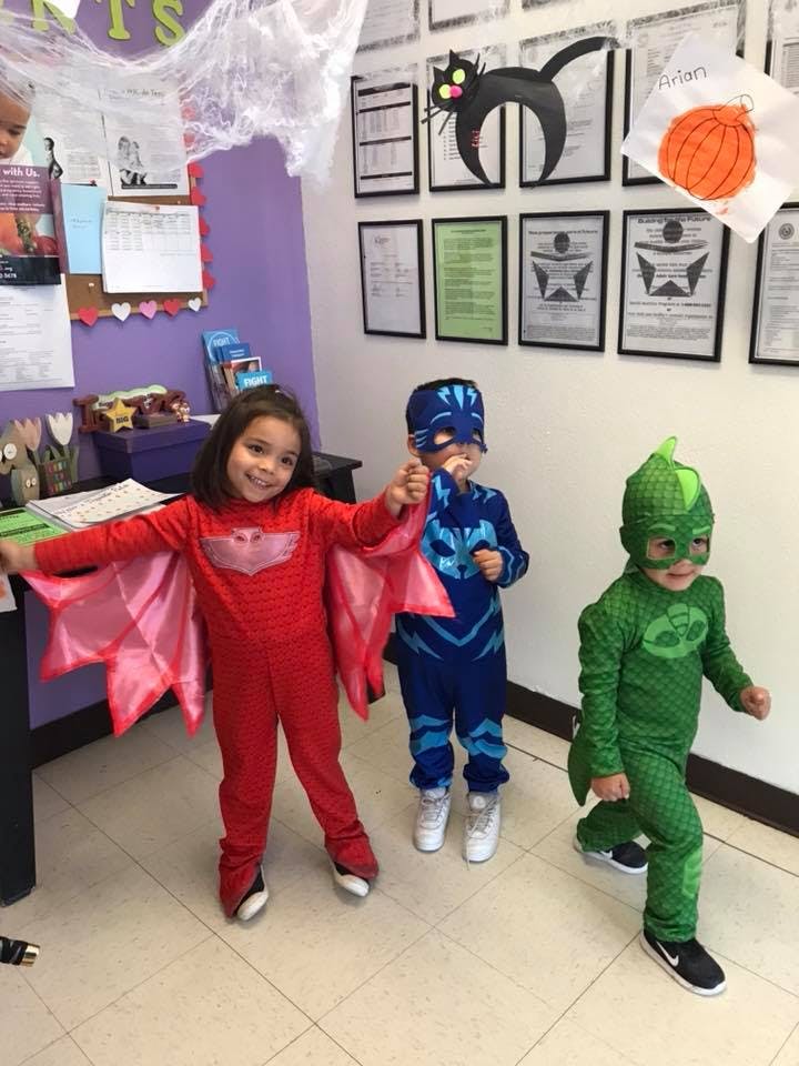 Three children in superhero costumes standing indoors