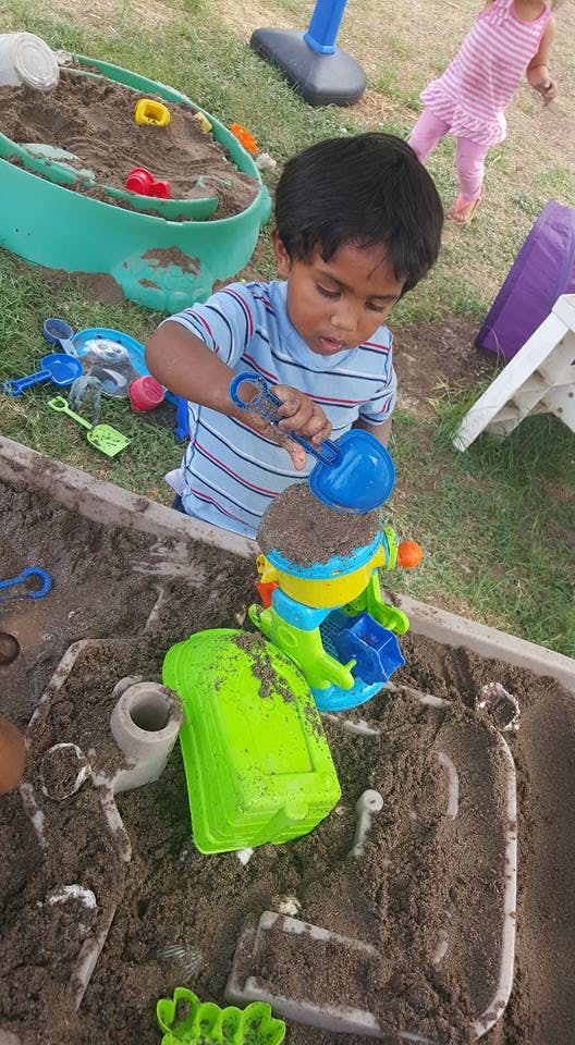 Child playing in a sandbox with a blue shovel and sand toys