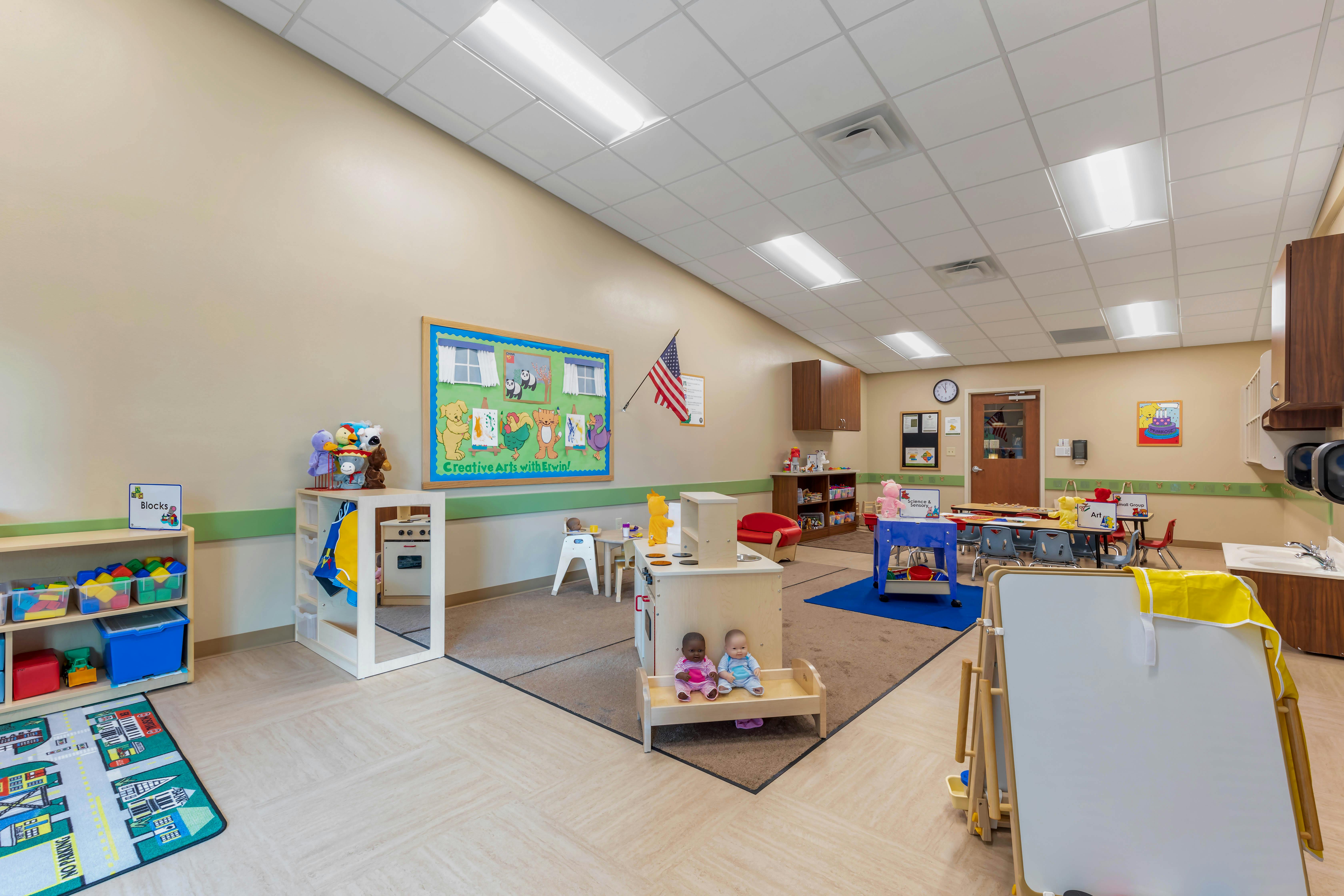 children's classroom with toys, play kitchen, small tables and chairs, and bulletin boards
