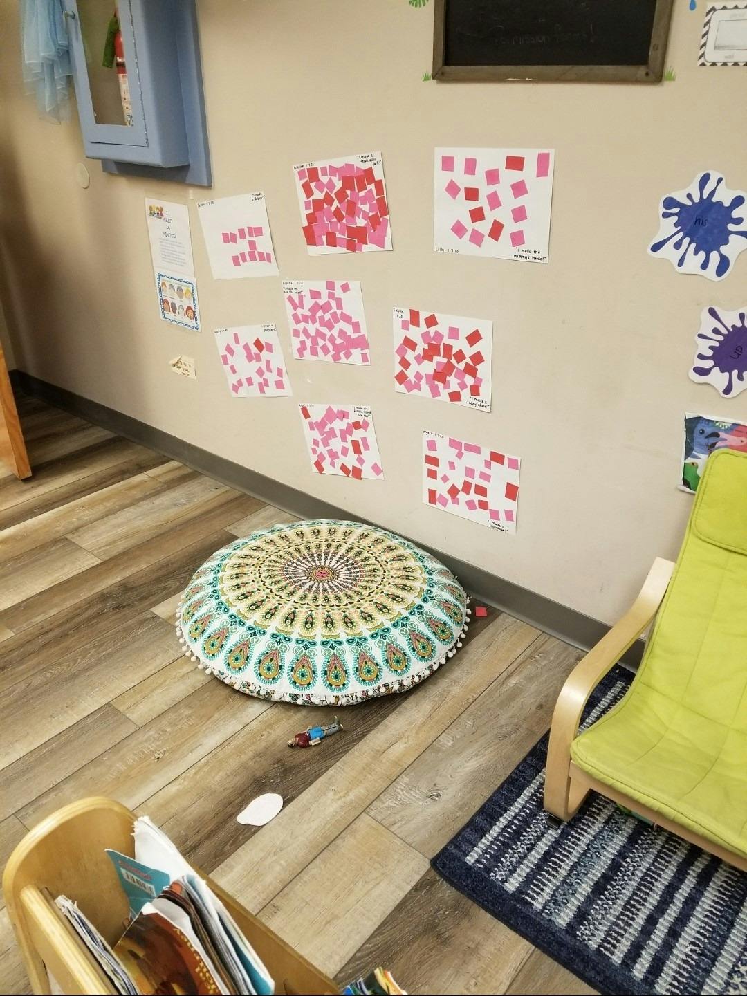 Wall with children's artwork, floor cushion, and chair