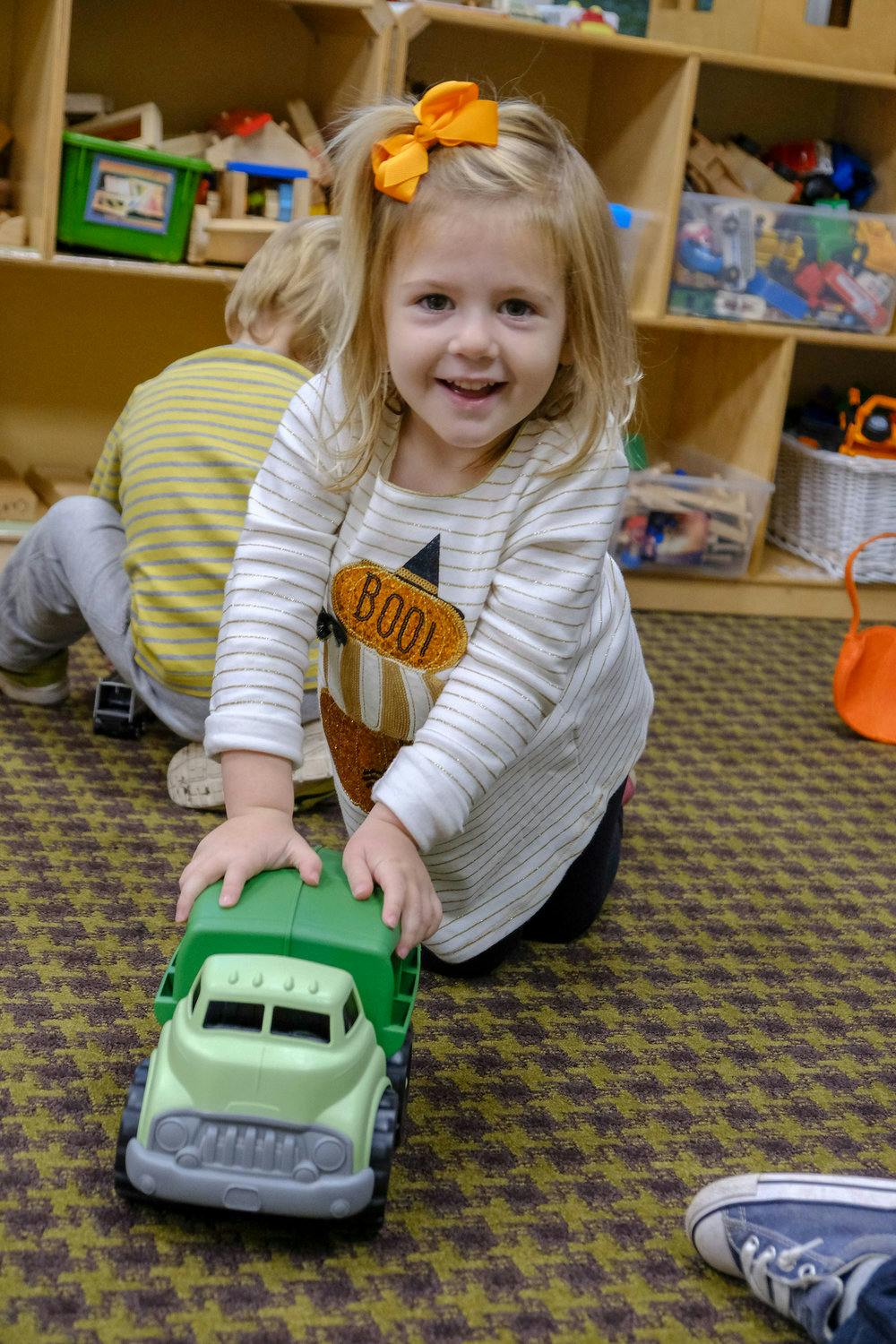 Child playing with a green toy truck on the floor
