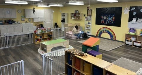 Childcare room with play areas and a person sitting on floor cushions