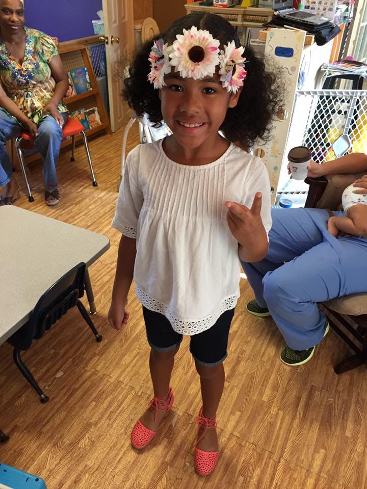 Child wearing a flower crown and white shirt, standing indoors
