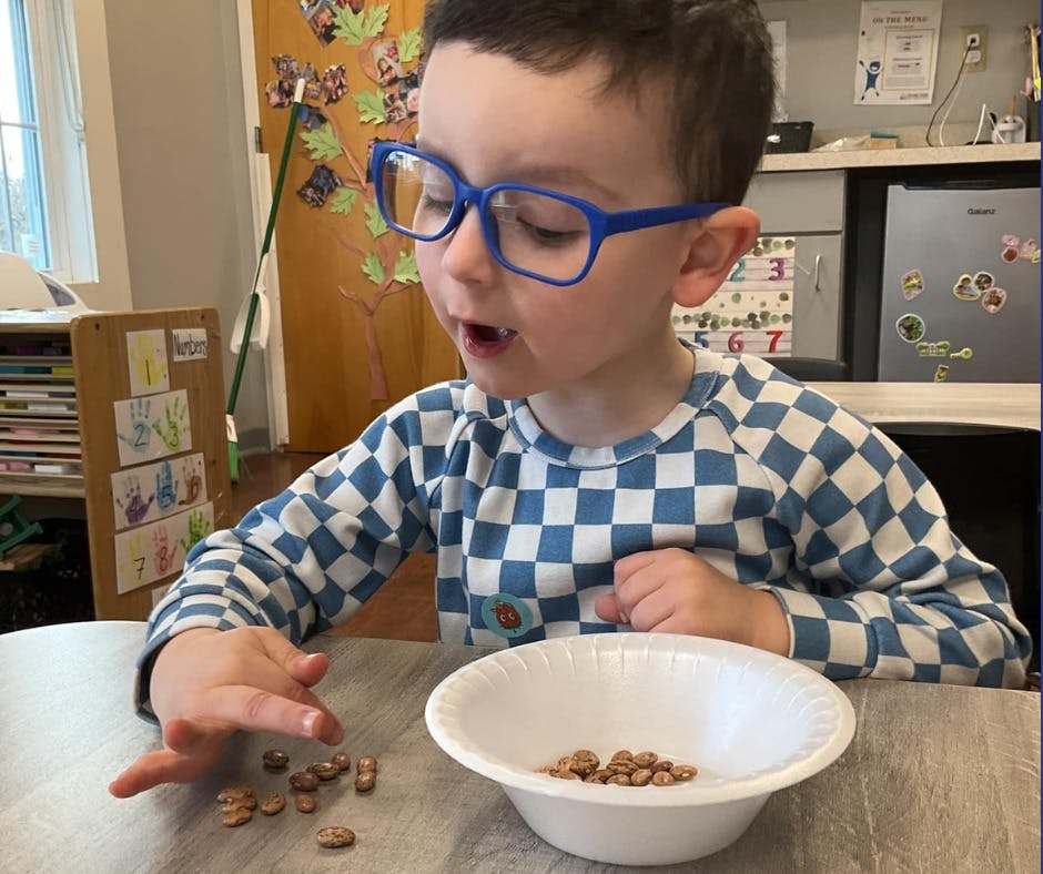Child in blue glasses playing with beans on a table