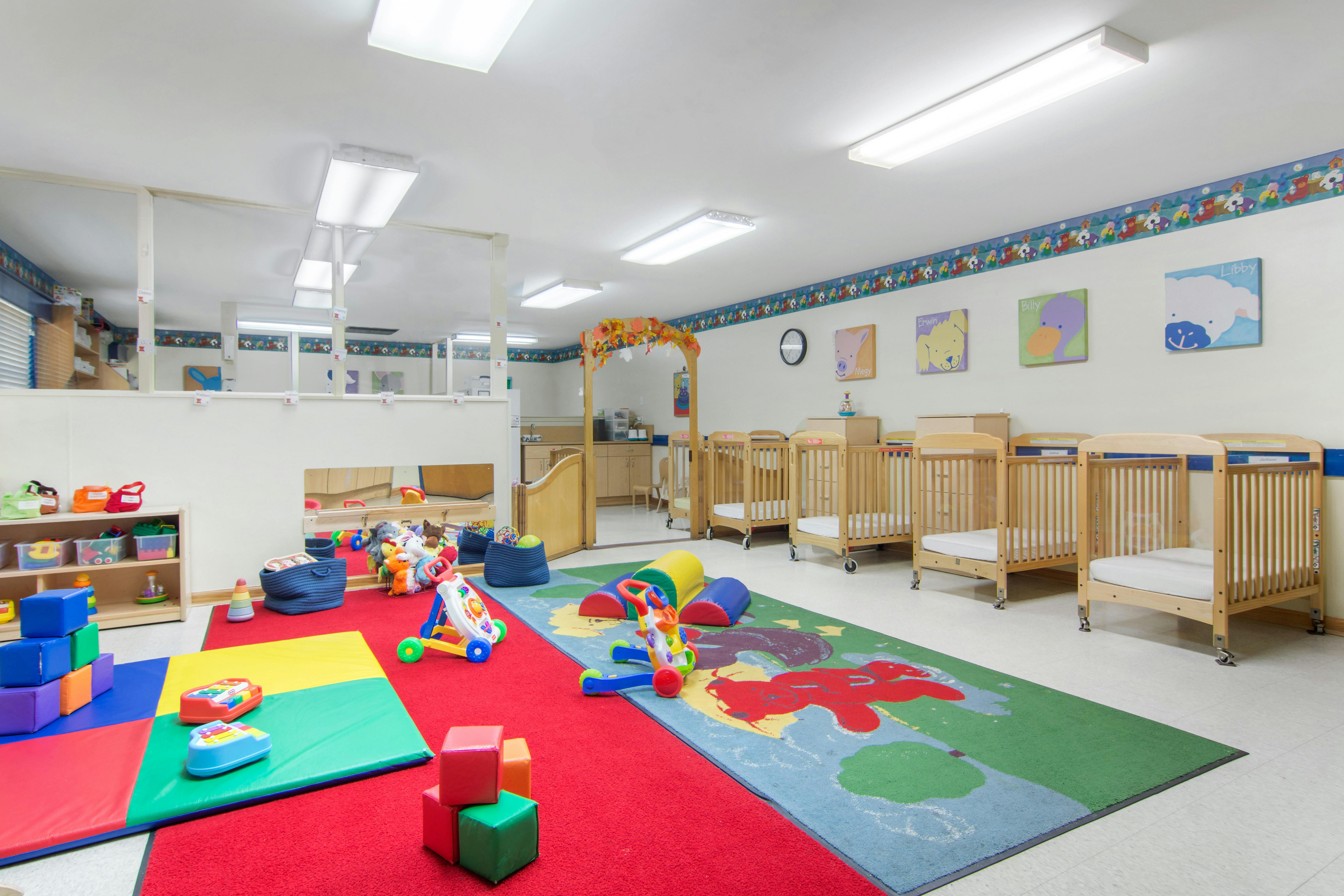A colorful childcare room with cribs, play mats, and children's toys