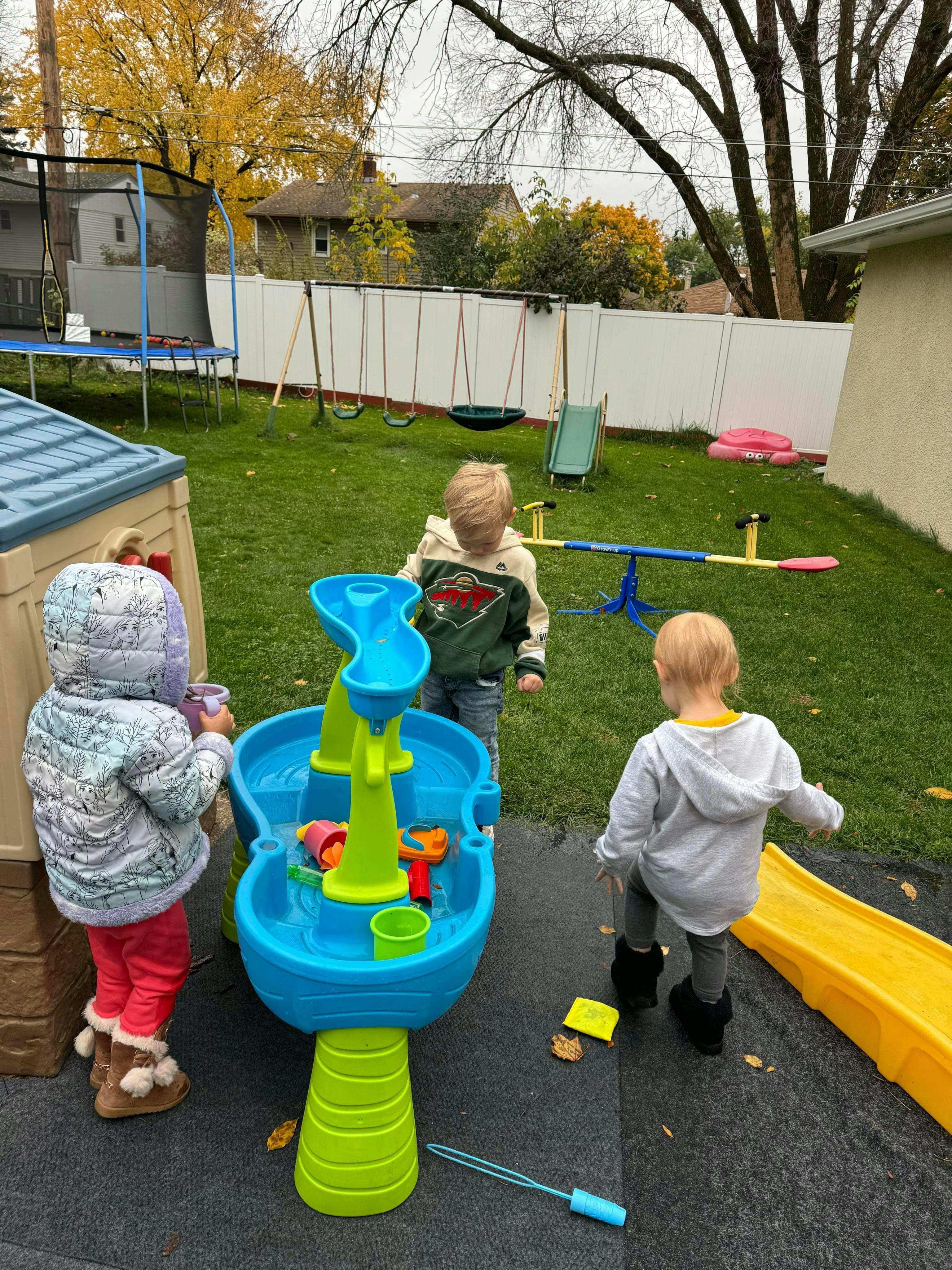 Three children playing with a water table in a backyard