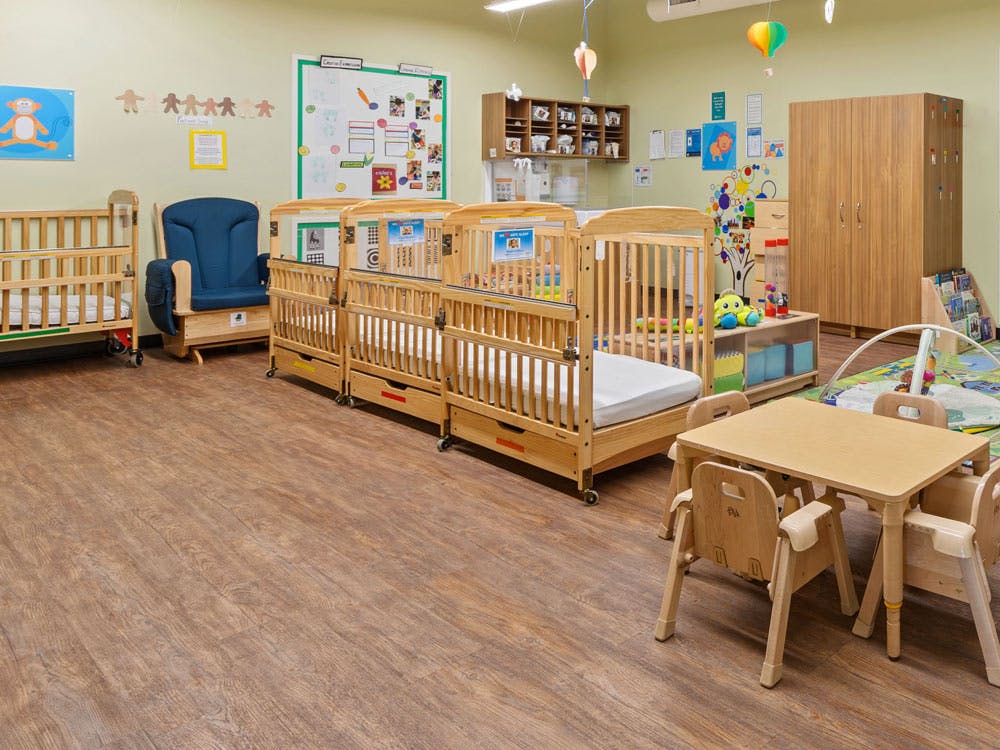 Cribs, small chairs, and a play mat in a childcare room