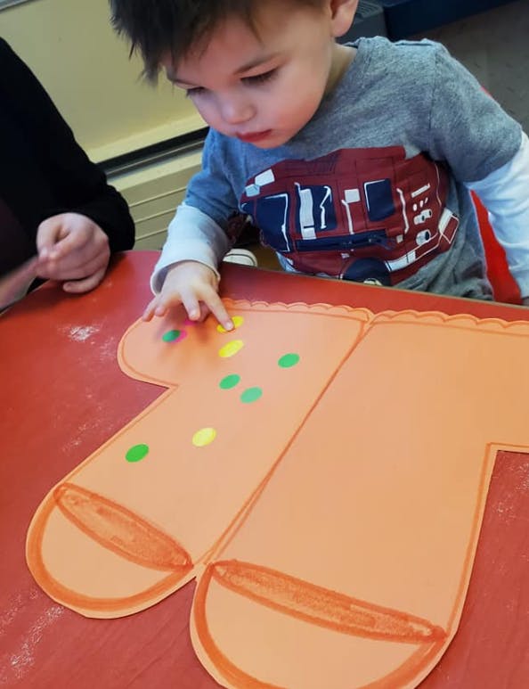 Child decorating a paper gingerbread person with colorful stickers