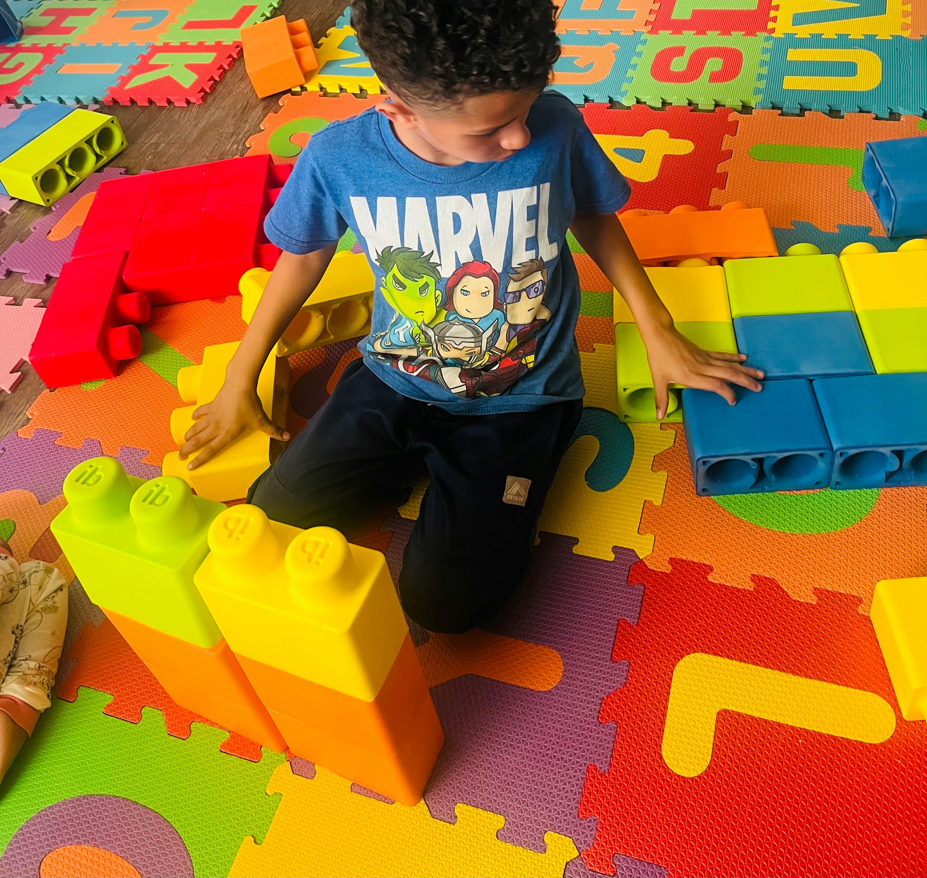 Child playing with large building blocks on a colorful mat