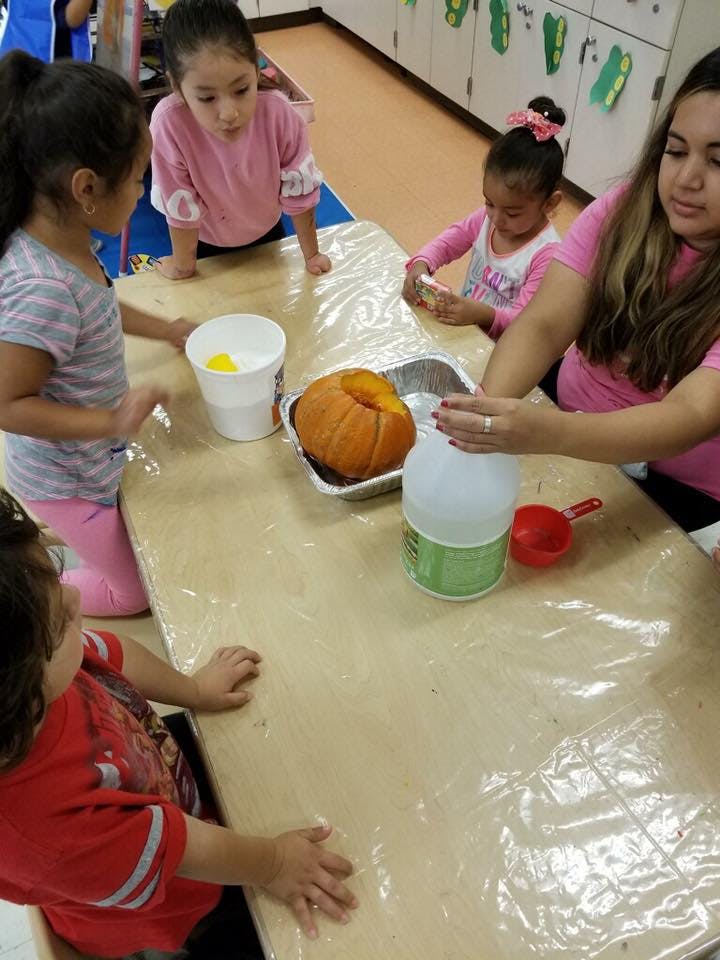 Adult and children around a table with a pumpkin and craft supplies