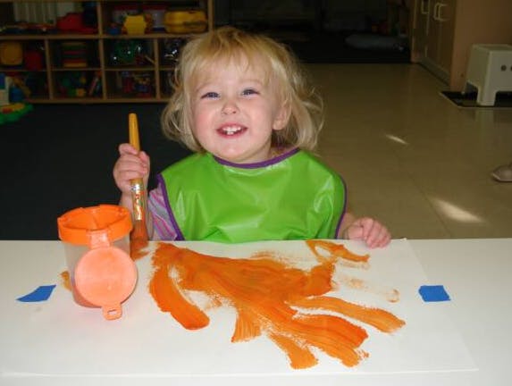 Child in a green smock painting with orange paint