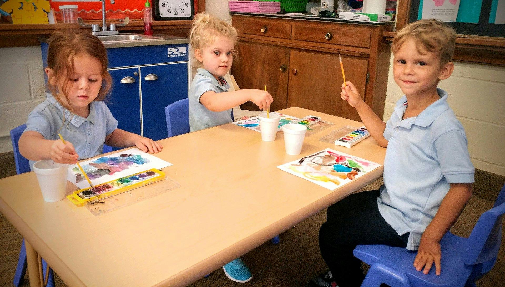Three children painting at a table in a classroom