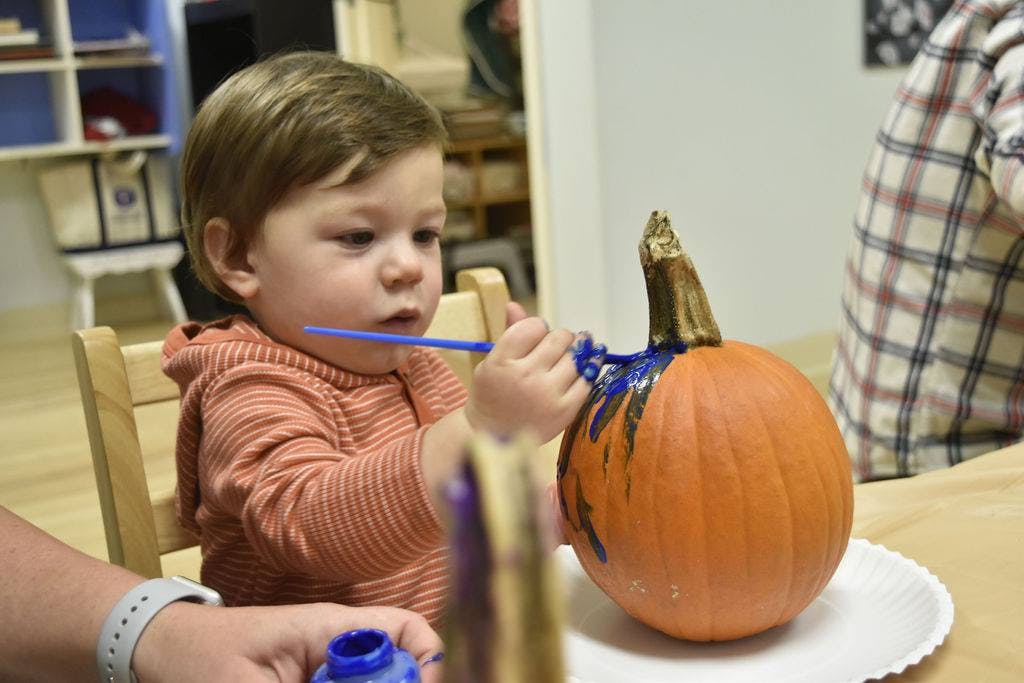 Child painting a pumpkin blue with a paintbrush