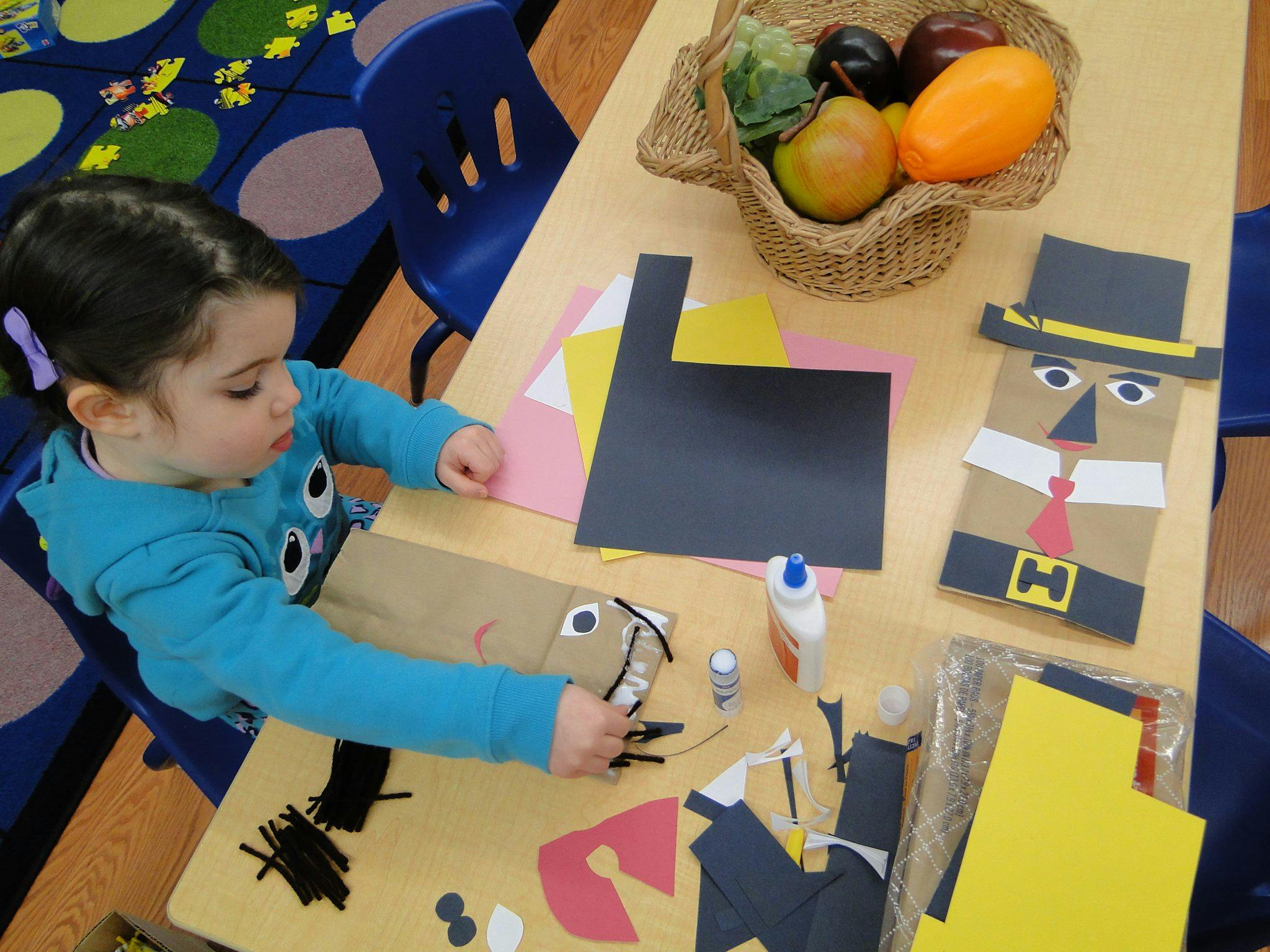 Child making a craft with paper and glue at a table