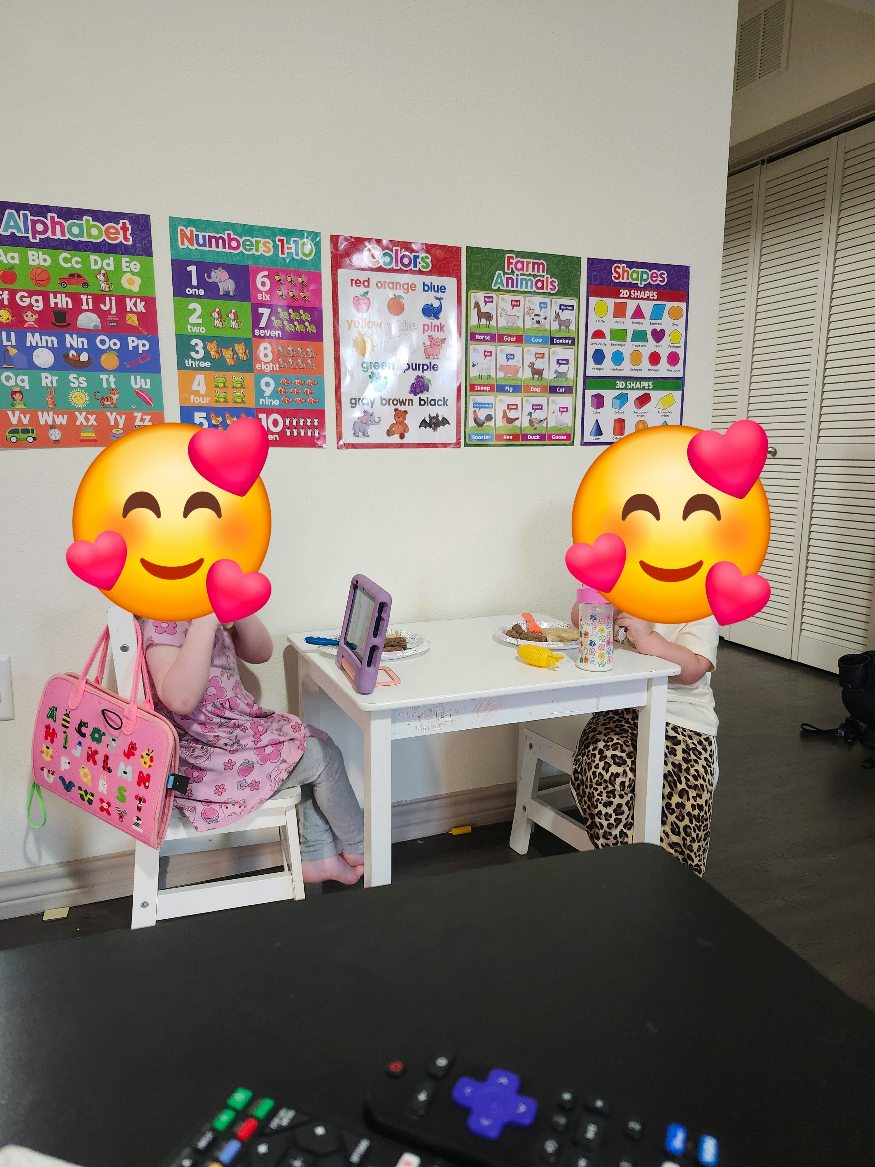 Two children sitting at a small table with educational posters on the wall