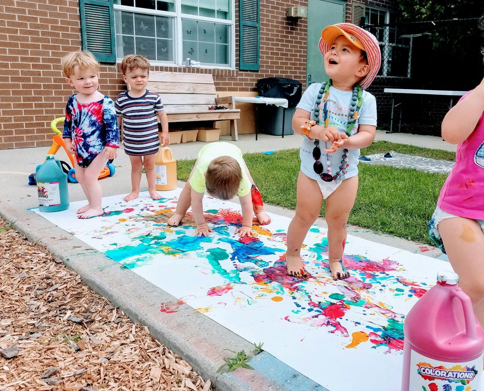 Children painting on a large white sheet outdoors