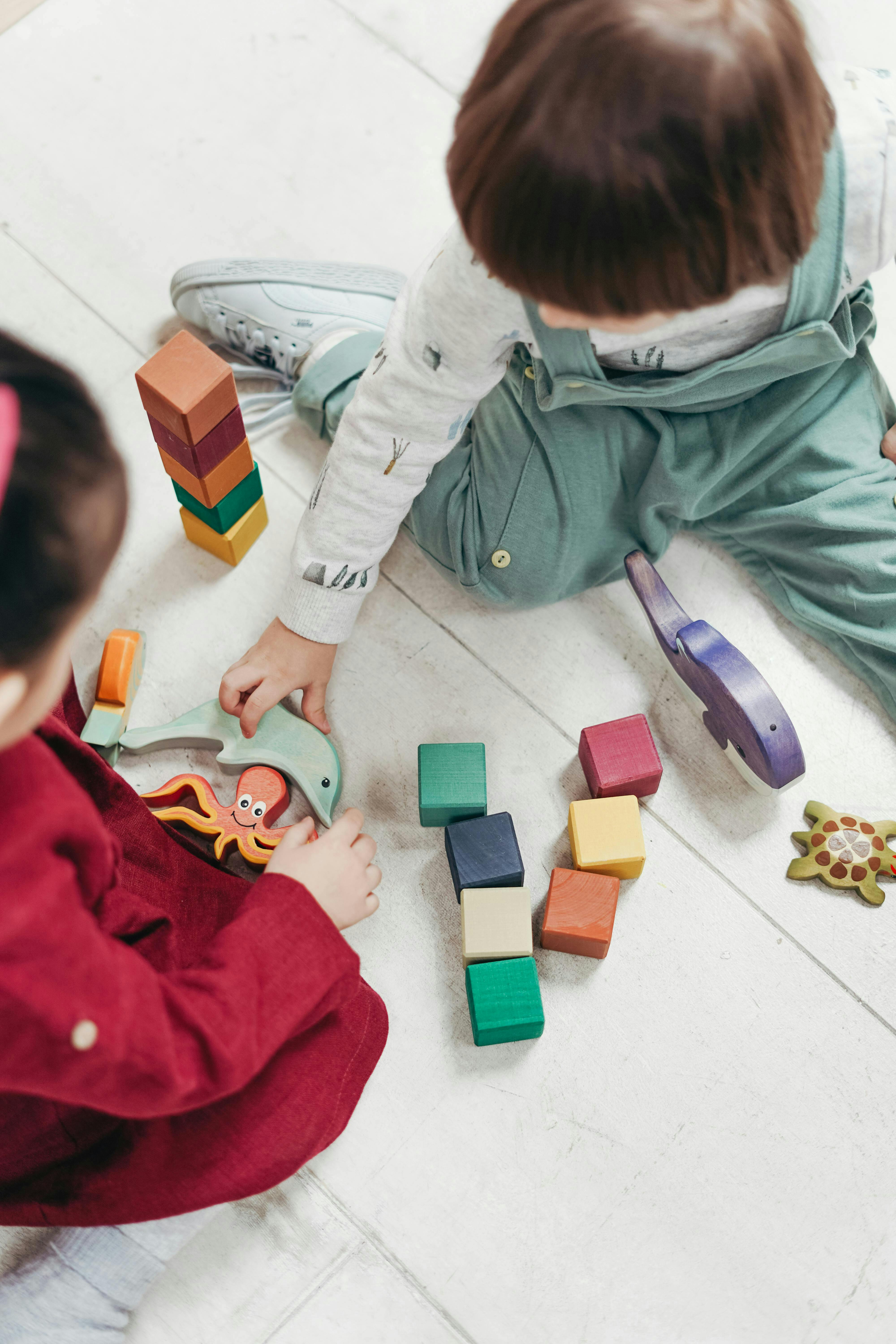 Two children playing with wooden blocks and toys on the floor