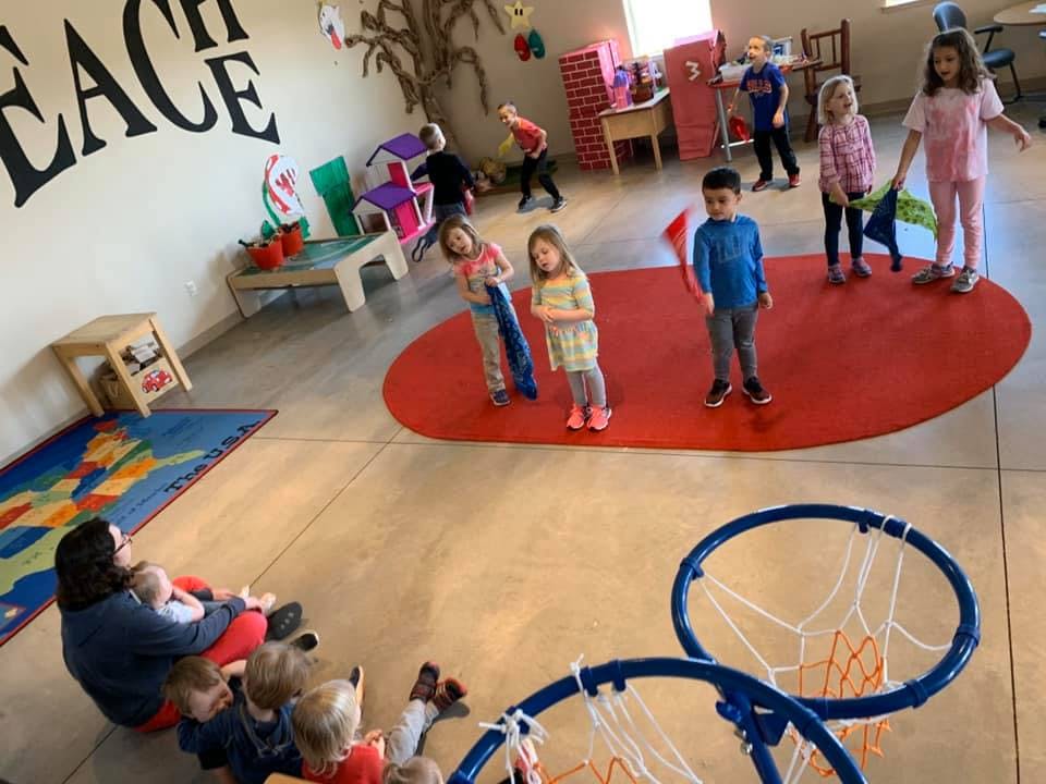 Children and adults in a large room with a red mat and basketball hoops