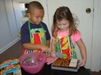 Two children in aprons cutting a cake