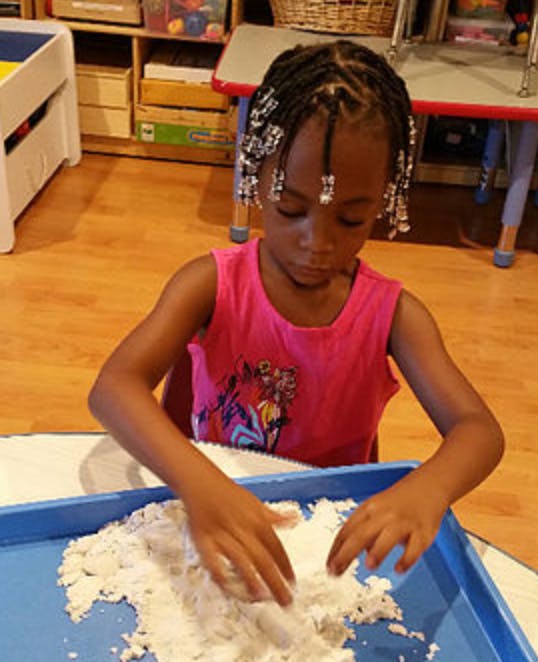 Child playing with sand in a blue tray