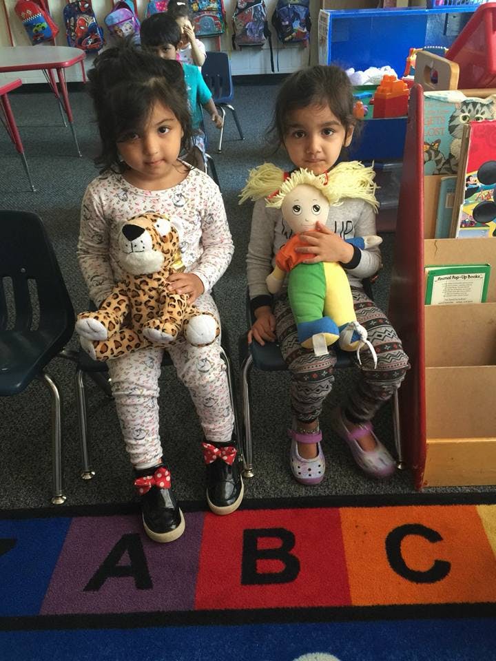 Two children sitting on chairs, each holding a stuffed toy