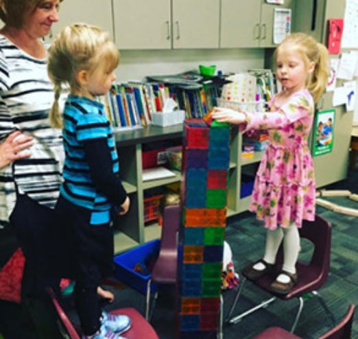 Adult and two children playing with colorful blocks in a classroom