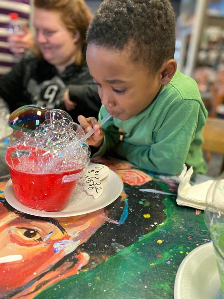 Child blowing bubbles into a red cup with a straw