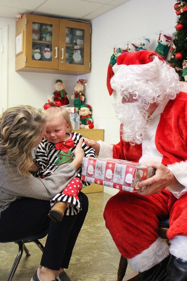 Person holding a child who is receiving a gift from Santa