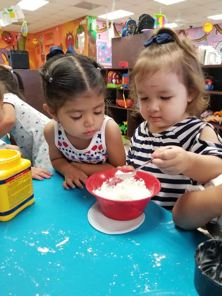 Two children mixing ingredients in a red bowl at a table