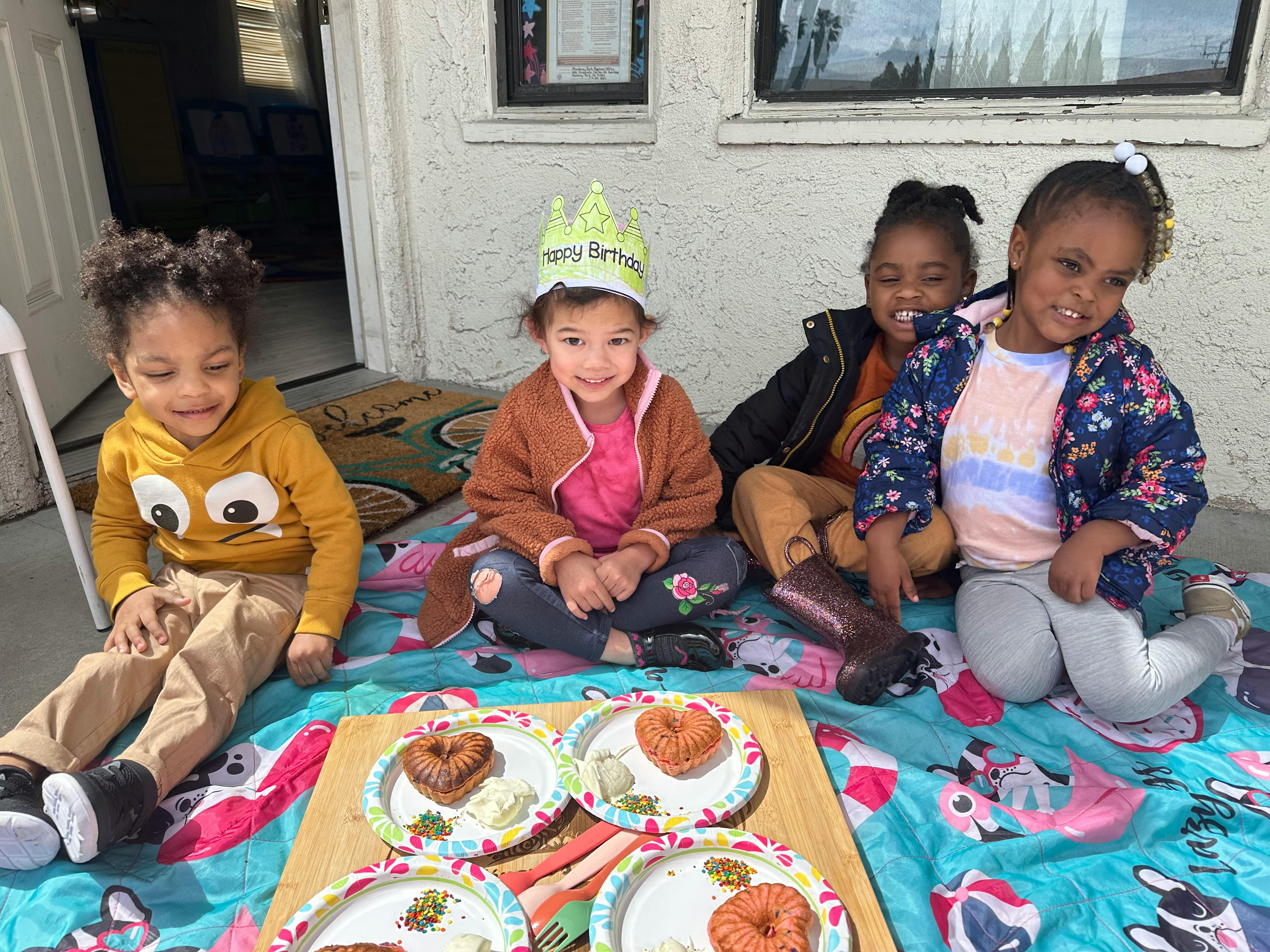 Four children sitting on a blanket with plates of food