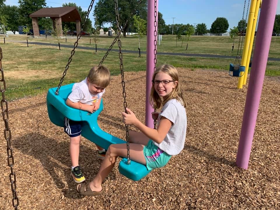 Child standing in a swing next to a teen sitting on a swing at a playground