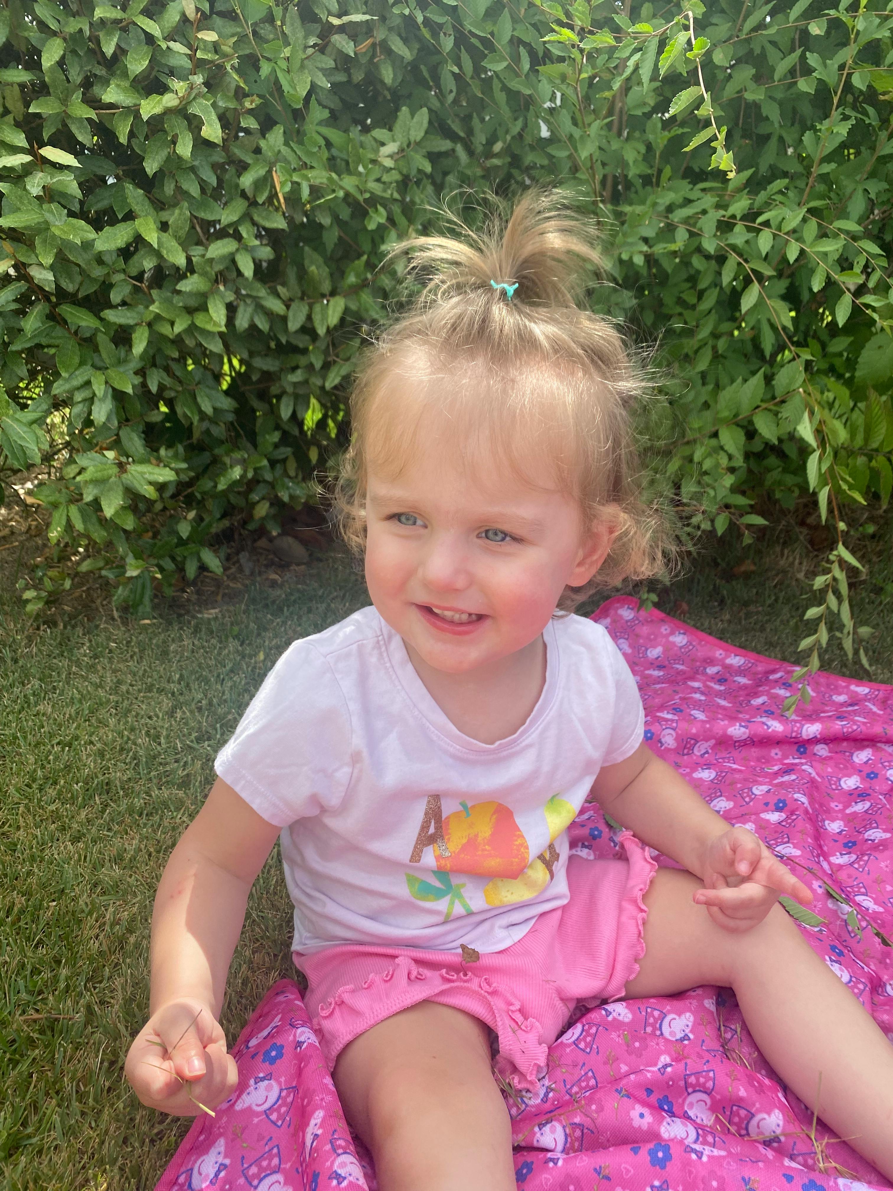 Child sitting on a pink blanket outdoors