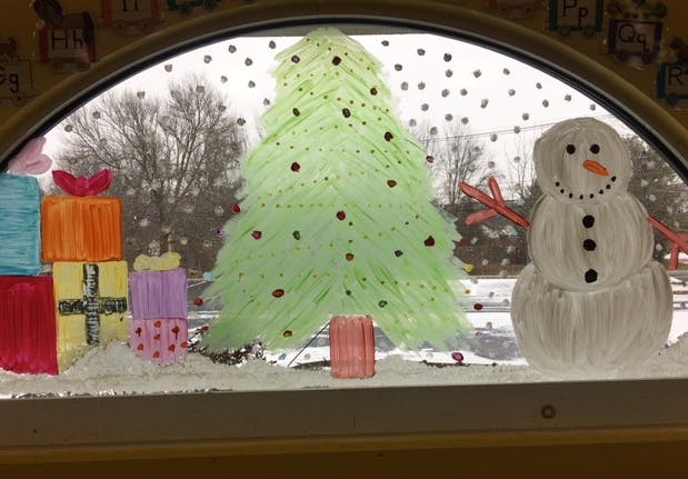 Window decorated with a paper Christmas tree, presents, and a snowman