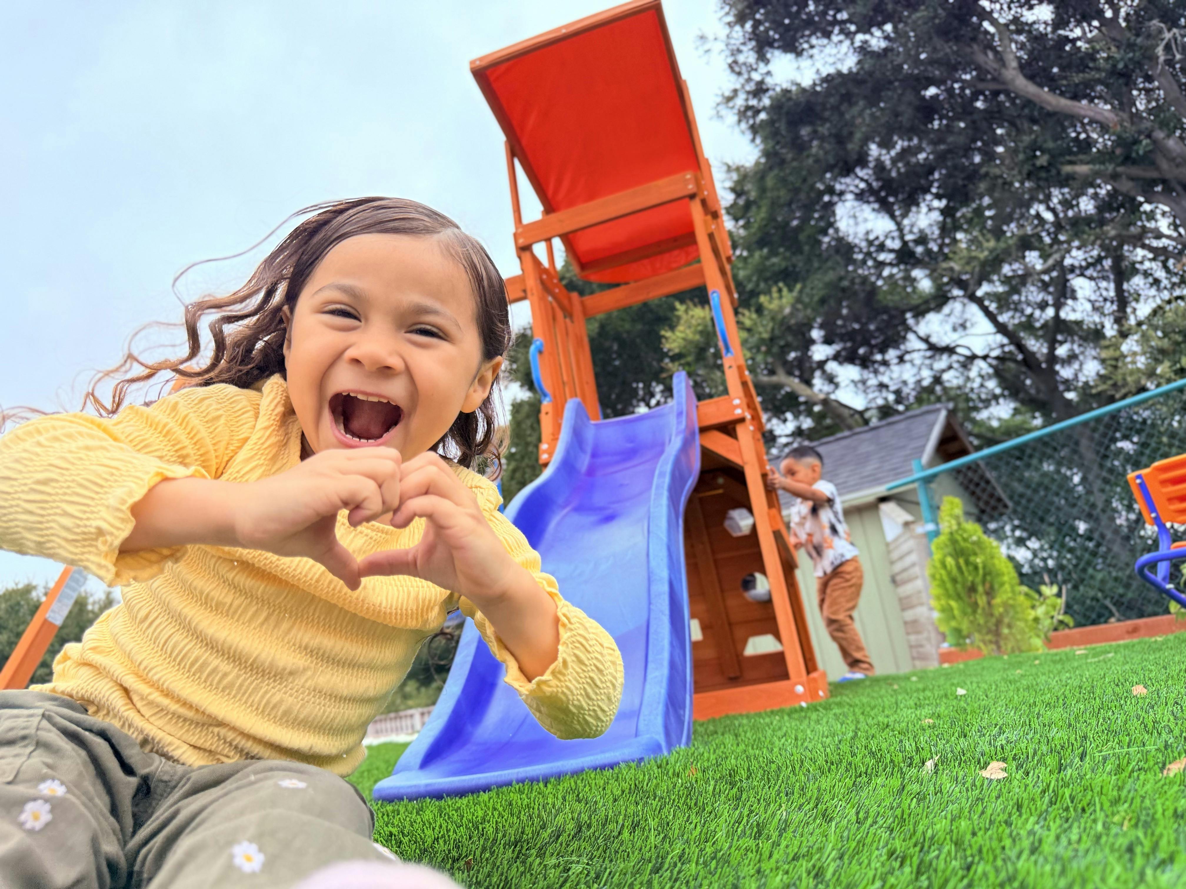 Child making a heart shape with hands on a playground