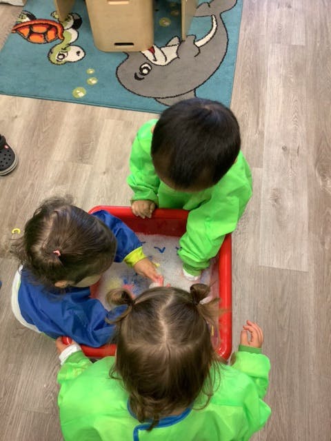Three children playing with water in a red bin