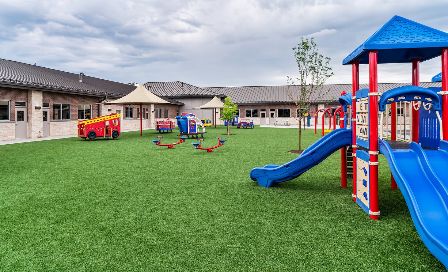 Playground equipment on a green field next to a school building