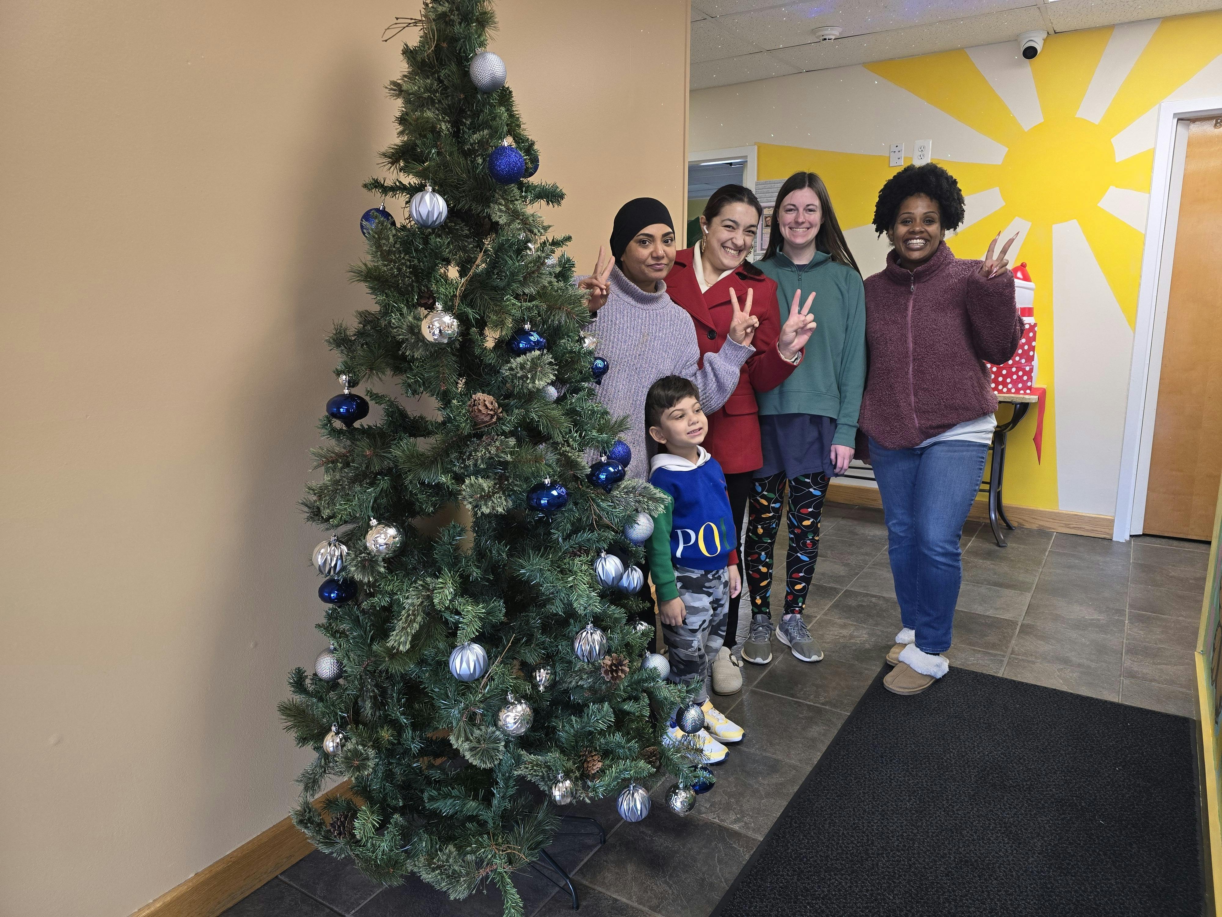 Four adults and one child posing around a Christmas tree, making peace signs