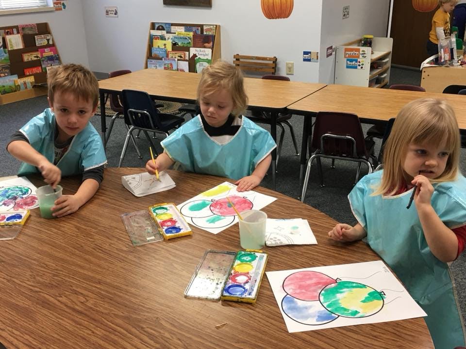 Three children painting at a table in a classroom