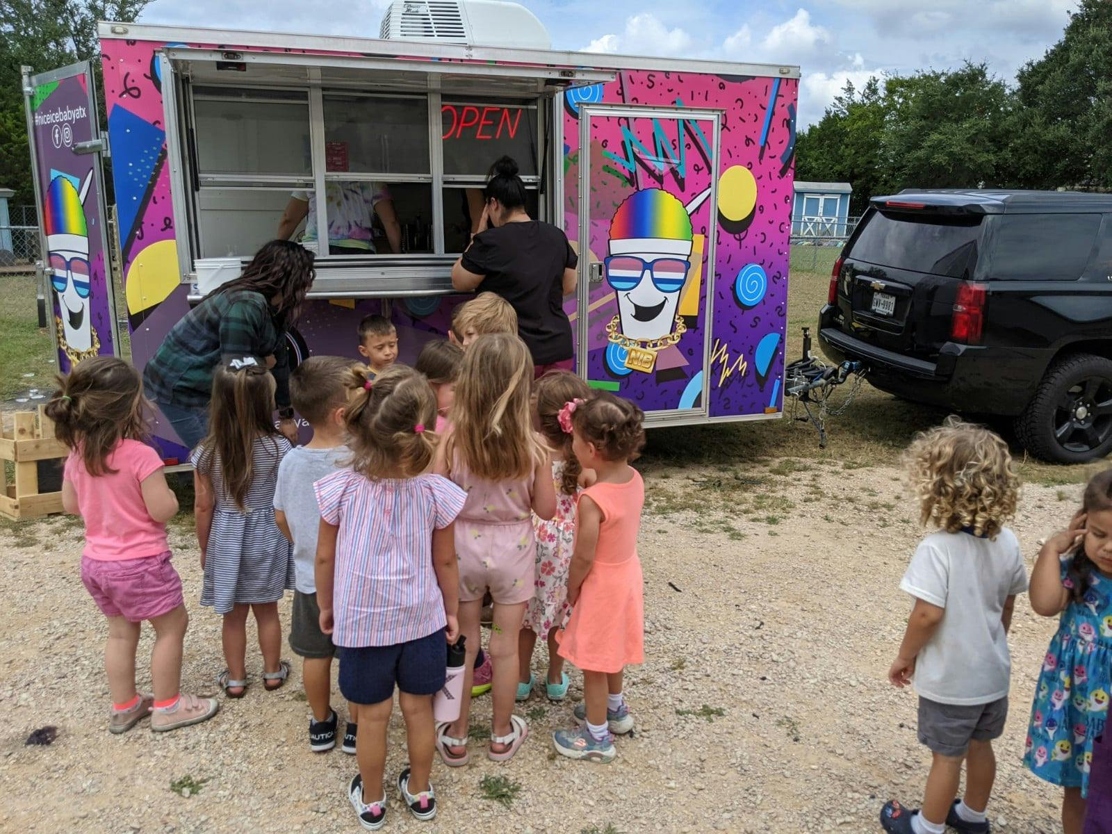 Children gathered around a food truck with people serving inside