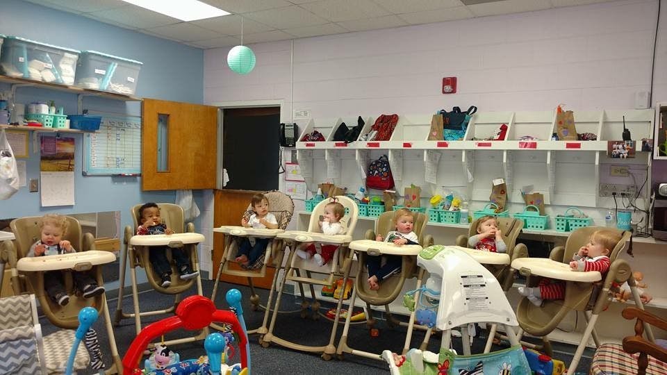 Multiple children sitting in high chairs in a classroom