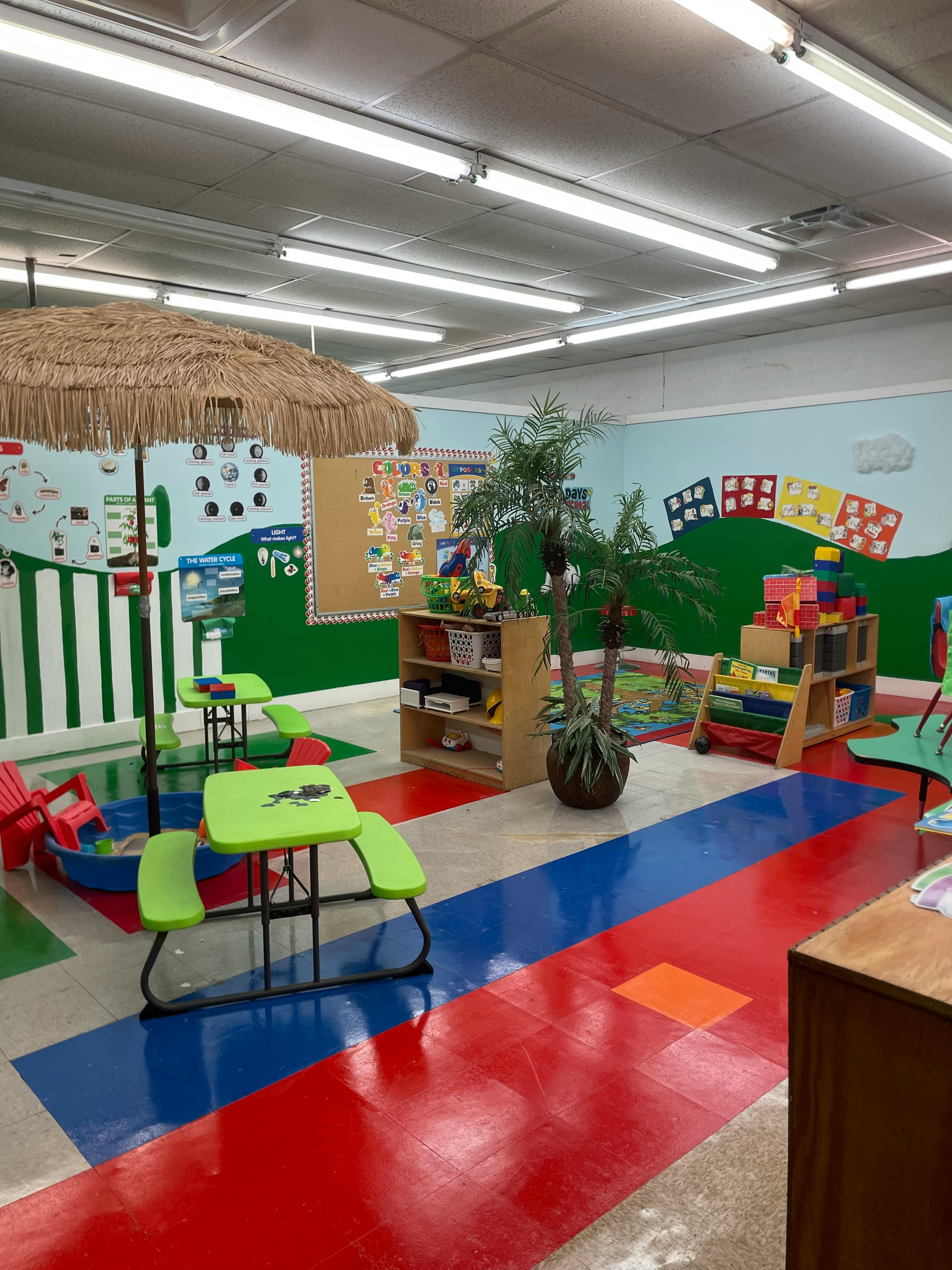 Classroom with colorful floor, small tables, and a straw umbrella