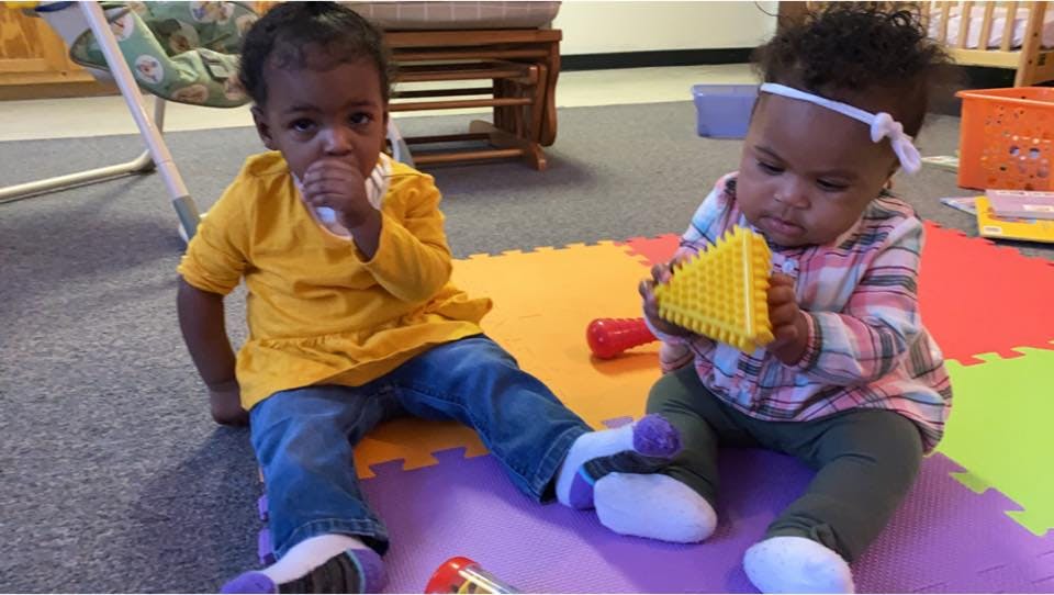 Two children sitting on a playmat, one holding a yellow toy
