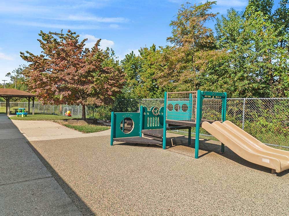An outdoor playground with a green and tan playset and slide