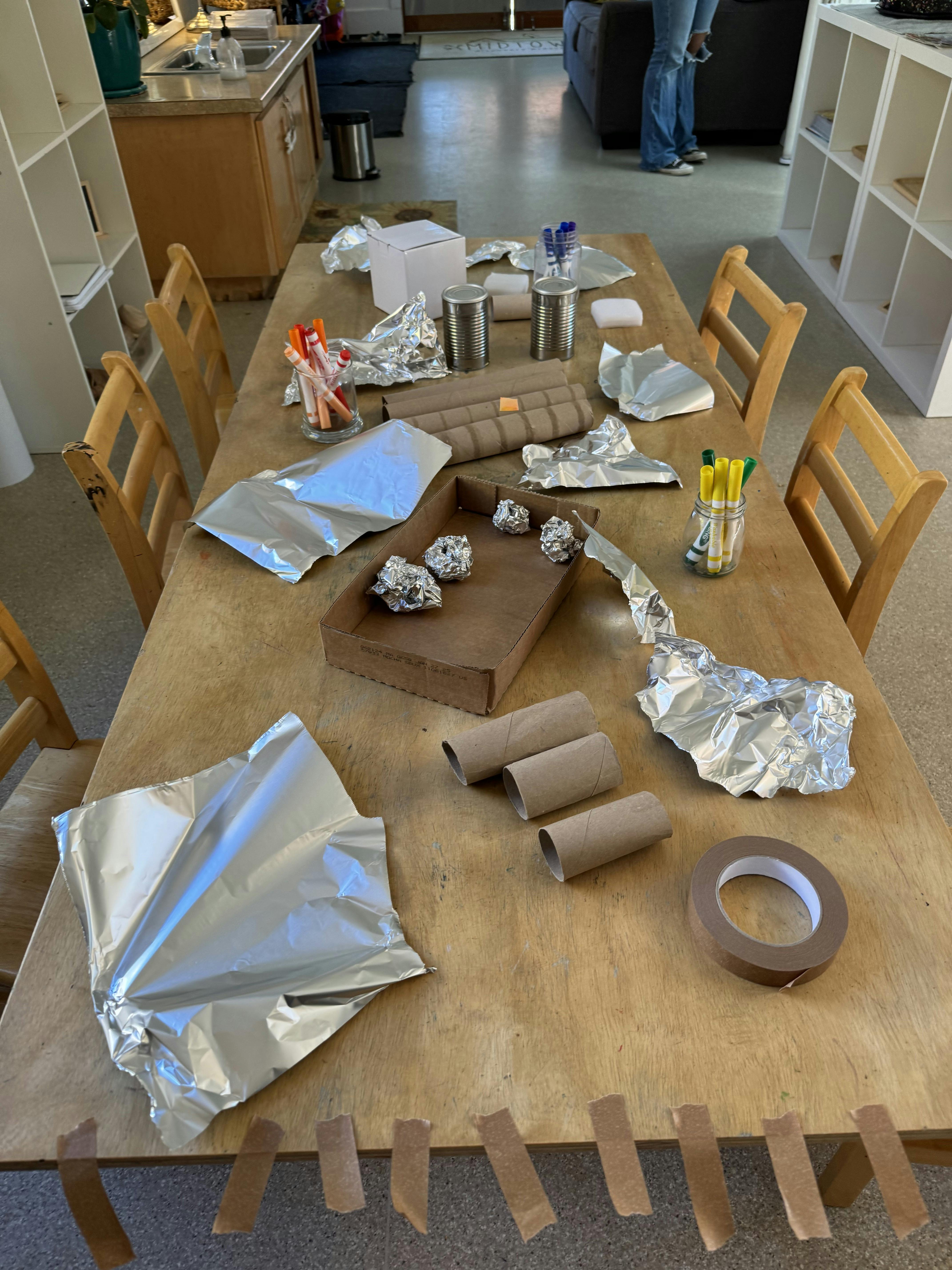 Craft supplies including foil, cardboard tubes, and markers on a wooden table
