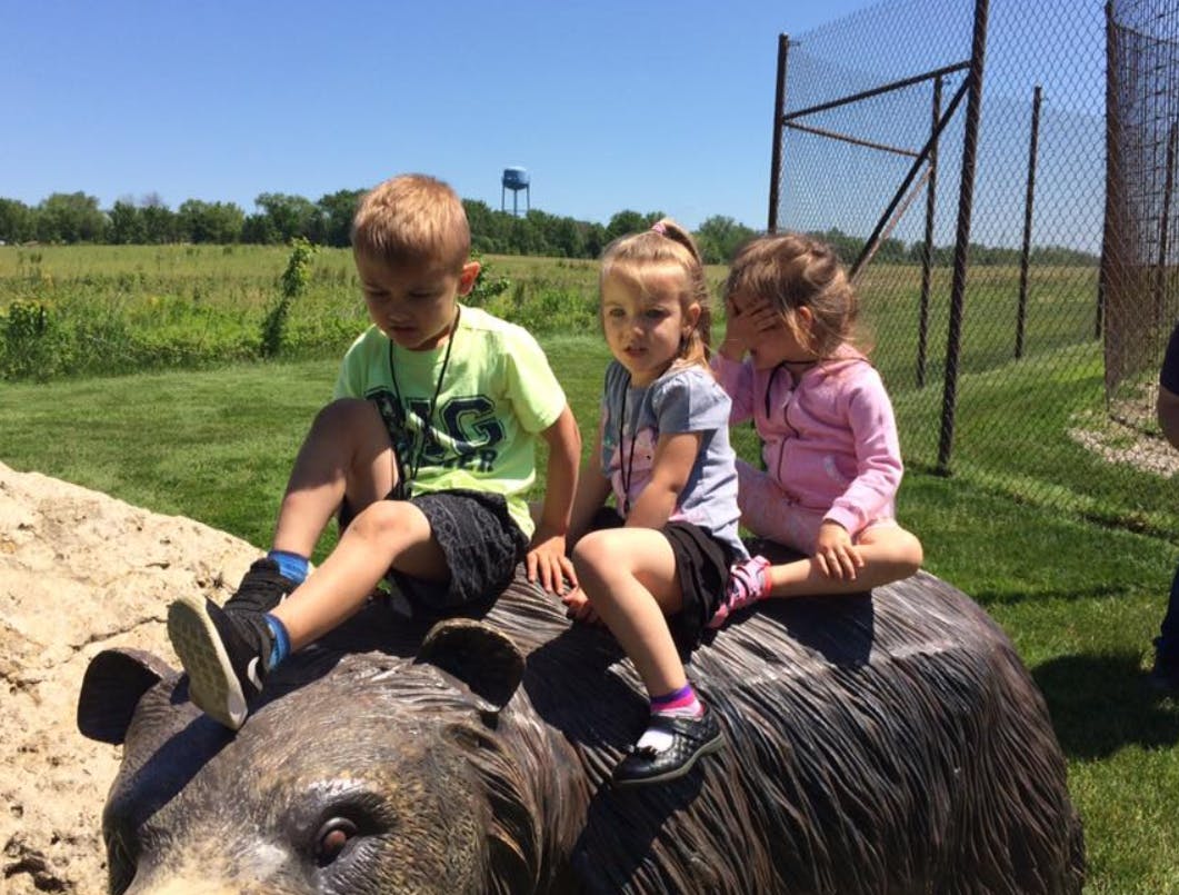 Three children sitting on a bear statue outdoors