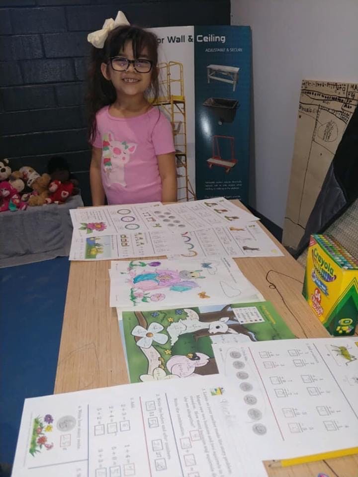 Child in glasses standing behind a table with papers