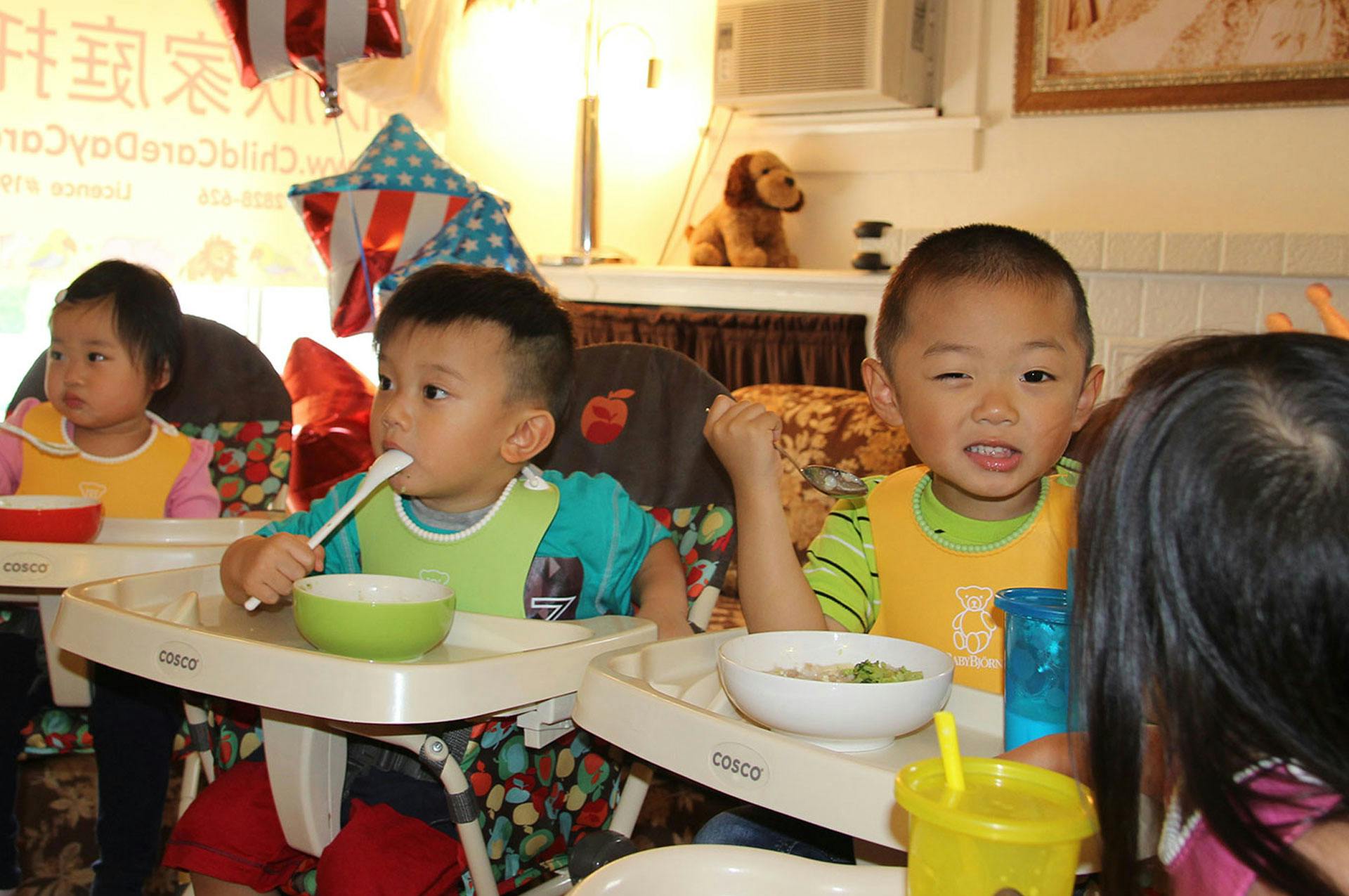 Three children in high chairs eating with spoons and bowls