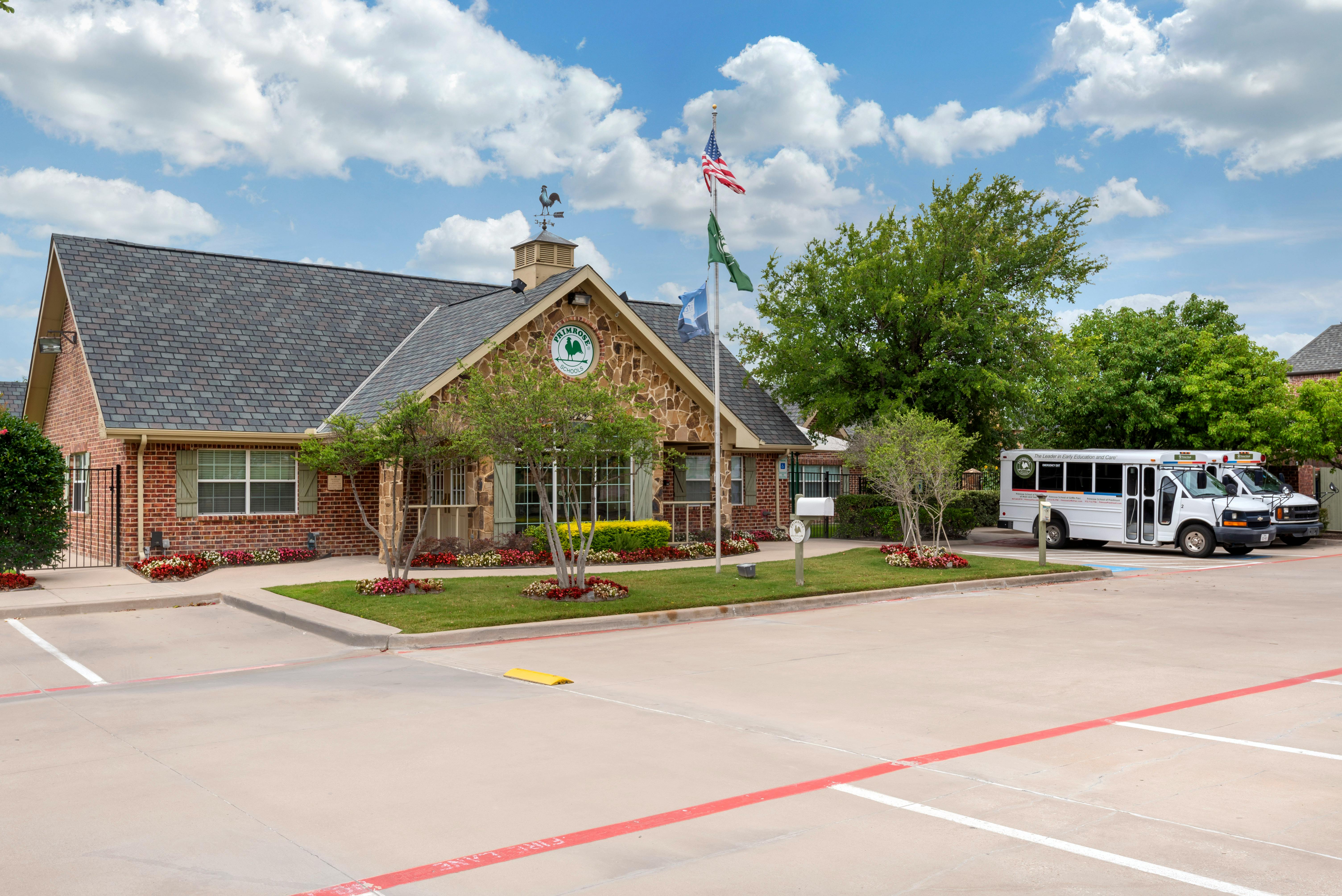 A school building with a Primrose Schools sign, US flag, and parked school buses